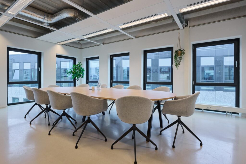 Moderne vergaderruimte op het John M. Keynesplein met ovale tafel, grijze stoelen en veel natuurlijk licht.